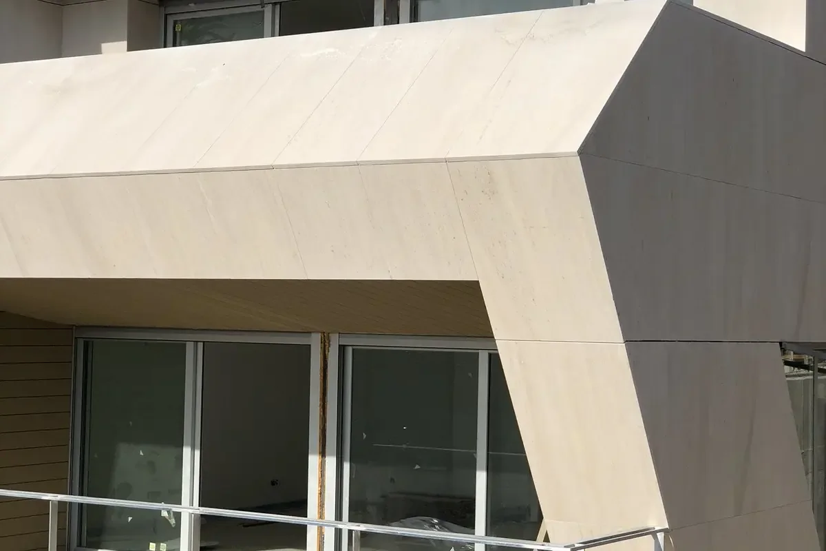 Aplacado terminado en volumen de fachada. Volumen de fachada en voladizo revestido con piezas grandes en tono crema de juntas finas sobre el ventanal de la terraza.