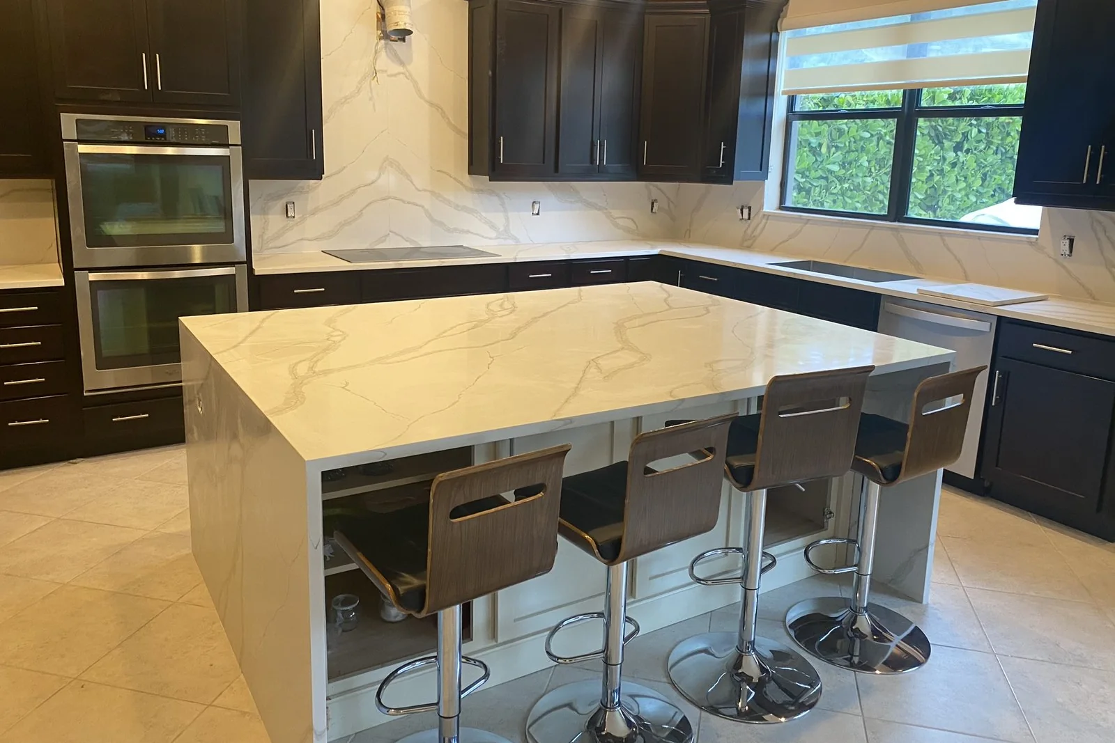 Isla de cocina con faldones y encimera blanca de veta gris, taburetes y el frontal de pared en la misma piedra