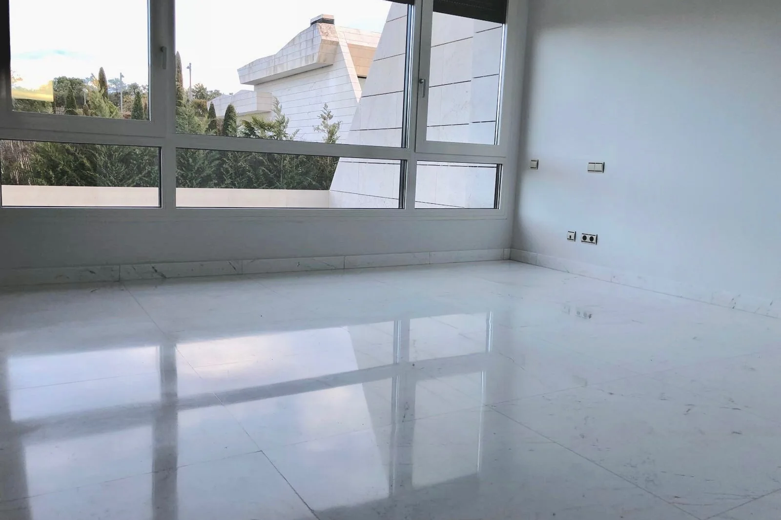 Estancia vacía con un ventanal corrido y el suelo blanco pulido reflejando la luz exterior