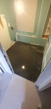 Pavimento oscuro visto desde la puerta. Suelo oscuro pulido con vetas blancas recién colocado, visto desde el umbral con las paredes de placa aún sin revestir.