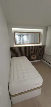 Dormitorio con cabecero de listones. Dormitorio individual con panel de listones en tono madera, espejo en hornacina iluminada y suelo claro en lamas.