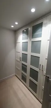 Armario empotrado de puertas blancas. Armario de puertas blancas con paneles translúcidos, techo con focos empotrados y suelo claro en lamas.