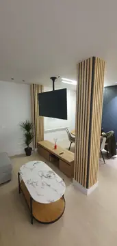 Salón con pilares forrados de listones. Salón con pilares revestidos de listones en tono madera, televisor colgado del techo y mesa de centro de tapa veteada.