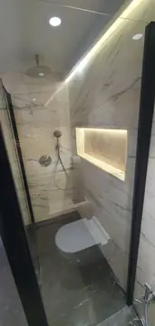 Interior de la ducha con hornacina. Paredes claras con veta gris en piezas grandes, hornacina iluminada, rociador de techo y grifería empotrada.
