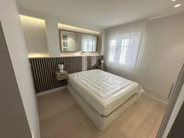 Dormitorio doble visto desde la puerta. Dormitorio con cama doble, panel de listones en tono madera, hornacinas iluminadas y ventana con estor claro.
