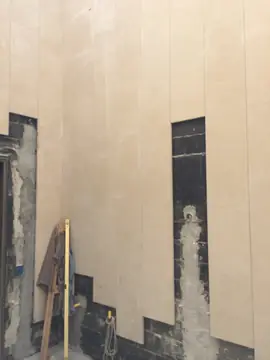 Aplacado en tono arena en colocación. Piezas verticales en tono arena colocadas de forma escalonada, con parte del muro de bloque negro todavía a la vista.