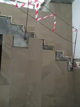 Aplacado del lateral de una escalera. Lateral de escalera revestido con piezas en tono arena recortadas siguiendo el perfil de los peldaños.