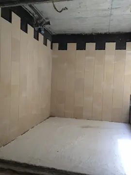 Estancia con paredes en tono arena. Paredes revestidas con piezas verticales en tono arena, con el remate superior pendiente y el techo aún en bruto.