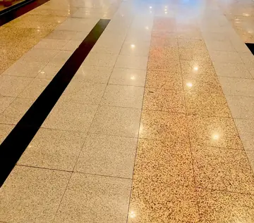 Pavimento pulido en franjas de dos tonos. Pasillo con franjas de piezas pulidas en tono claro y moteado dorado, separadas por una banda negra.