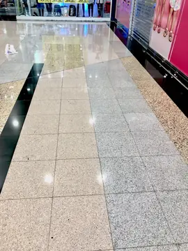 Franjas de pavimento en tres tonos. Pavimento pulido con franjas de piezas claras, grises y moteadas entre bandas negras junto a los escaparates.