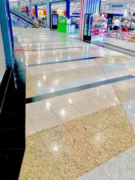 Franjas cruzadas en el pavimento. Pavimento pulido con franjas de piezas claras, grises y moteadas atravesadas por bandas negras en la entrada a una zona comercial.