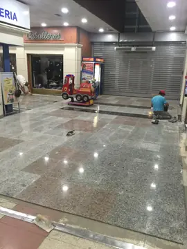 Pavimento nuevo durante la colocación. Colocación del pavimento pulido gris moteado con recuadros rosados y franja negra mientras se rematan los bordes.