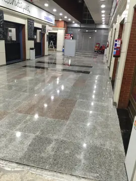 Pasillo comercial con pavimento nuevo. Pasillo entre locales con pavimento pulido gris moteado, recuadros rosados y franjas negras.