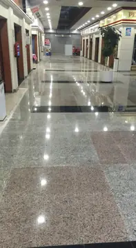 Galería comercial con pavimento pulido. Galería con pavimento pulido gris moteado y recuadros rosados que se prolonga hasta el fondo del pasillo.