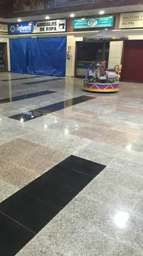 Plaza interior con franja negra. Pavimento pulido gris moteado con recuadros rosados atravesado por franjas negras en una plaza entre locales.