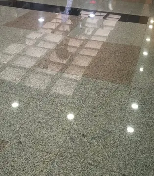 Detalle del pavimento gris con recuadro rosado. Losas pulidas en gris moteado con un recuadro rosado y una franja negra al fondo, con el reflejo de las luces del techo.