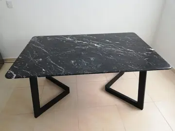 Mesa con sobre negro de vetas blancas. Sobre negro pulido con vetas blancas y esquinas redondeadas sobre patas metálicas negras en V.