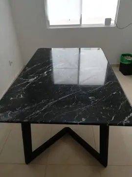 Mesa negra de veta blanca junto a la ventana. Sobre negro pulido con vetas blancas que refleja la luz de la ventana, sobre estructura metálica.