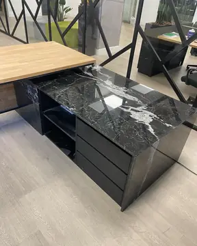 Mesa de despacho con sobre negro veteado. Módulo de despacho forrado en negro con vetas blancas, con cajonera y ala de tablero en tono madera.