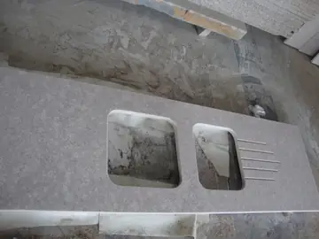 Encimera moteada con huecos de seno y escurridor. Encimera gris rosada moteada con huecos de seno y ranuras de escurridor, sobre el suelo del taller.