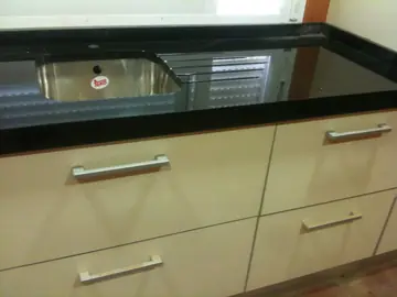 Encimera negra con fregadero bajo encimera. Encimera negra pulida con seno de acero bajo encimera y escurridor ranurado sobre muebles crema.