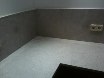 Rincón de encimera y frontal grises. Encuentro en esquina de encimera y frontal de grano gris, con enchufe empotrado en el aplacado.
