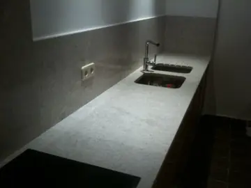 Encimera gris con fregadero doble bajo encimera. Tramo de encimera de grano gris con fregadero doble de acero bajo encimera y frontal del mismo tono.