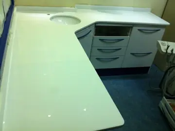 Encimera blanca en L con lavabo. Encimera blanca pulida en L con lavabo bajo encimera y copete, sobre muebles de una consulta.