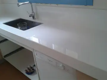 Encimera blanca con fregadero bajo encimera. Encimera blanca pulida con seno de acero bajo encimera, pendiente de montar puertas.