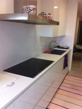 Cocina lineal blanca con placa y fregadero. Encimera blanca continua con placa y fregadero, frontal claro y muebles sin tiradores.