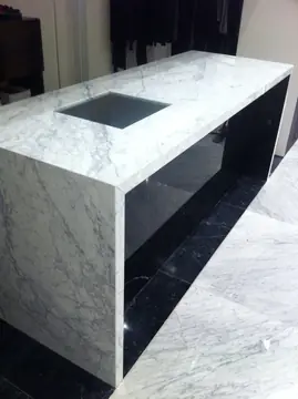 Mostrador blanco veteado en tienda. Mostrador blanco de veta gris con costados hasta el suelo e interior negro, sobre pavimento de piezas blancas y negras.