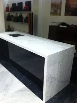 Mostrador veteado visto desde el otro lado. Mostrador blanco de veta gris con caída hasta el suelo e interior negro, en una tienda.