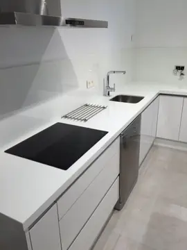 Cocina blanca con placa y seno bajo encimera. Encimera y frontal blancos pulidos con placa, seno bajo encimera y muebles sin tiradores.