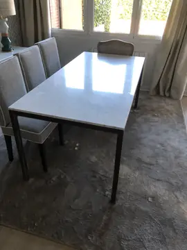 Mesa de comedor con tablero blanco pulido. Mesa de comedor con tablero blanco de veta suave sobre estructura metálica oscura.