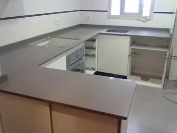 Cocina en U con encimera gris lisa. Encimera gris lisa en forma de U ya colocada, con los muebles aún pendientes de puertas.