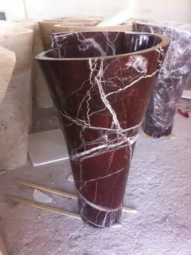 Lavabo de pie rojo con vetas blancas. Lavabo de pie cónico rojo con vetas blancas, entre otras piezas en el taller.