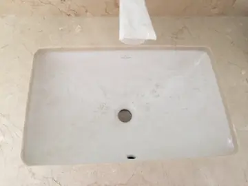 Lavabo bajo encimera en tono crema. Detalle del lavabo blanco encastrado bajo una encimera en tono crema con veta suave.