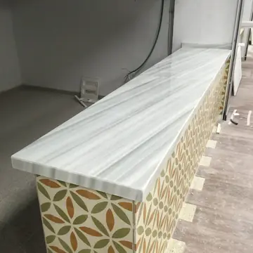 Mostrador con encimera blanca veteada. Mostrador de puesto con encimera blanca de veta gris lineal y frente de baldosa con dibujo de hojas.