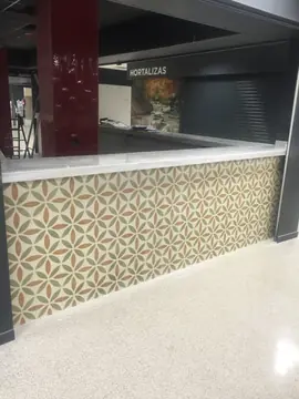 Mostrador en esquina de puesto. Mostrador en esquina con encimera blanca veteada y frente de baldosa con dibujo de hojas.