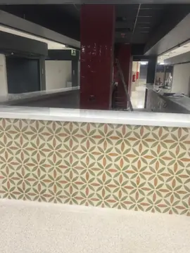 Mostrador frontal junto a pilar rojo. Frente de baldosa con dibujo de hojas y encimera blanca veteada en un puesto junto a un pilar de azulejo rojo.