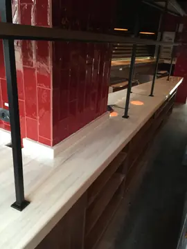 Barra con encimera blanca y postes negros. Barra con encimera blanca de veta suave, postes metálicos negros y pared de azulejo rojo.
