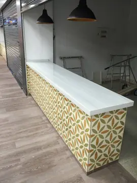 Mostrador con encimera blanca y frente decorado. Mostrador con encimera blanca veteada y frente de baldosa con dibujo de hojas, con el puesto aún sin equipar.