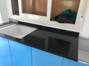 Encimera negra brillante con hueco de fregadero. Encimera negra pulida con el hueco del fregadero recortado, sobre muebles con film azul de protección.