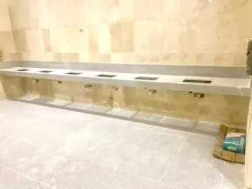 Encimera corrida con huecos de lavabos. Encimera gris moteada con huecos para lavabos en fila, sobre una pared aplacada en tono crema.