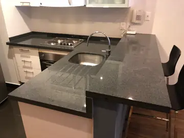 Cocina con península y barra gris oscura. Península con encimera gris oscura moteada, escurridor ranurado y barra elevada con taburetes.