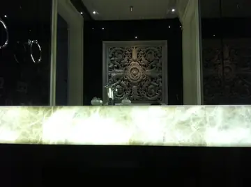 Frente retroiluminado de encimera de lavabo. Frente de encimera translúcido iluminado desde dentro, ante un espejo que refleja un panel tallado.