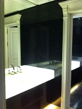 Encimera de lavabo retroiluminada. Encimera de lavabo iluminada desde dentro, con grifería de tres piezas y paredes oscuras con veta blanca.