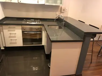 Cocina en L con encimera gris oscura. Cocina en L con encimera gris oscura moteada, placa, fregadero bajo encimera y barra elevada.