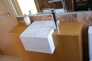 Lavabo cúbico sobre mueble en tono madera. Lavabo cúbico en tono crema con ranuras en cruz, volado sobre un mueble en tono madera.