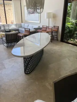 Mesa con tapa ovalada en el salón. Tapa ovalada blanca con veta suave y canto texturizado sobre base de celosía, en un salón abierto al jardín.